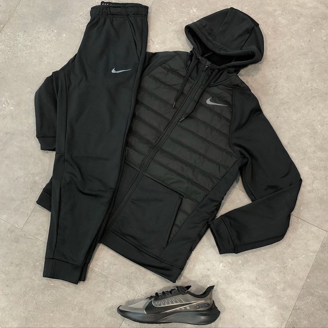 Black Nike hooded jacket, sweatpants, and athletic sneakers laid out on a grey tiled floor.