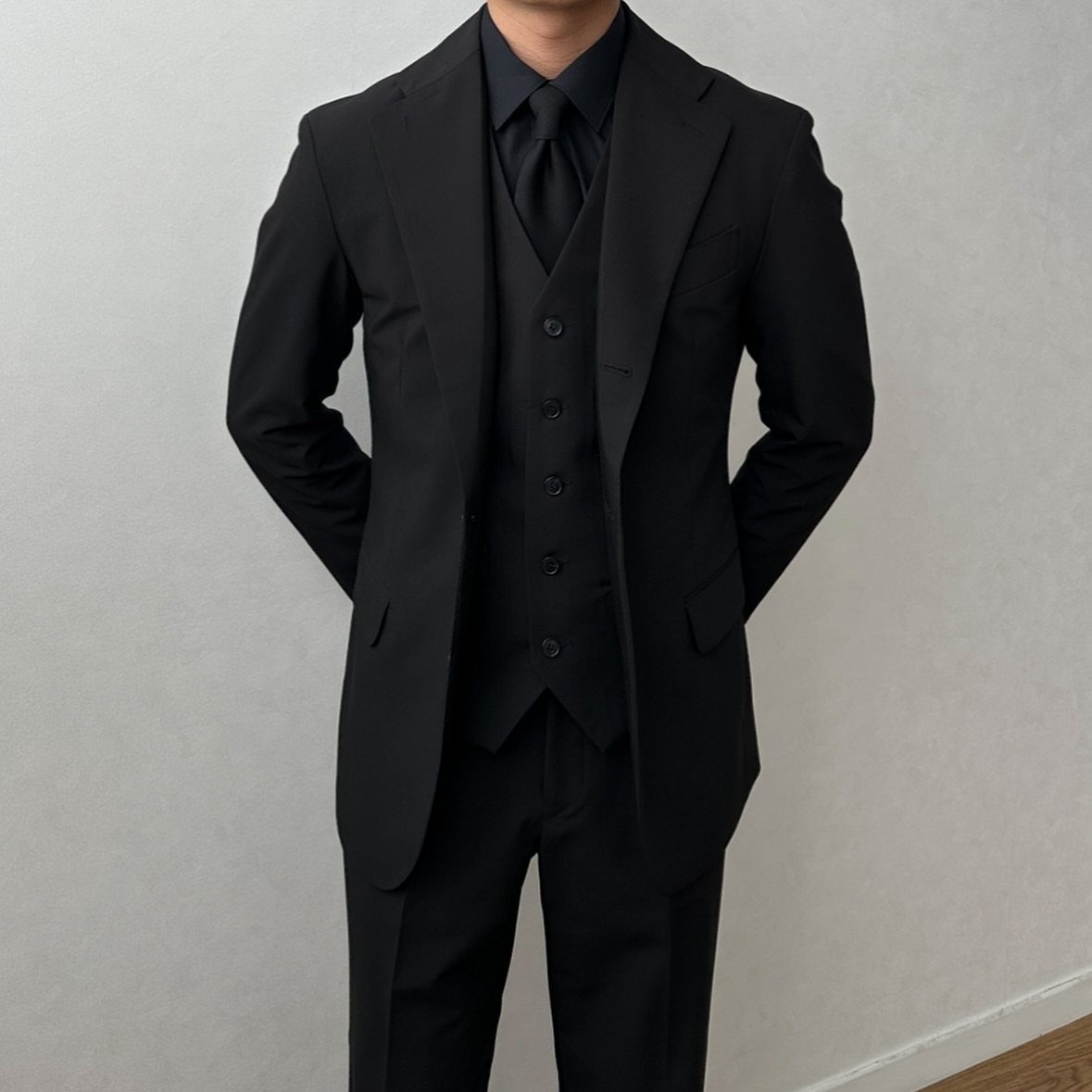A person wearing a formal black three-piece suit with a blazer and waistcoat.