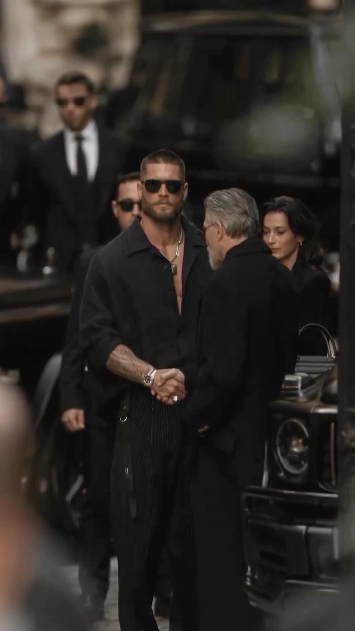 A man wearing an all black outfit with sunglasses and a button-down shirt.