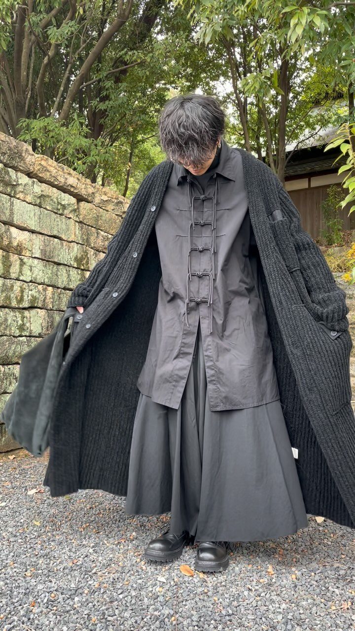 Person wearing an all-black outfit with a long cardigan, buttoned shirt, and wide maxi skirt.