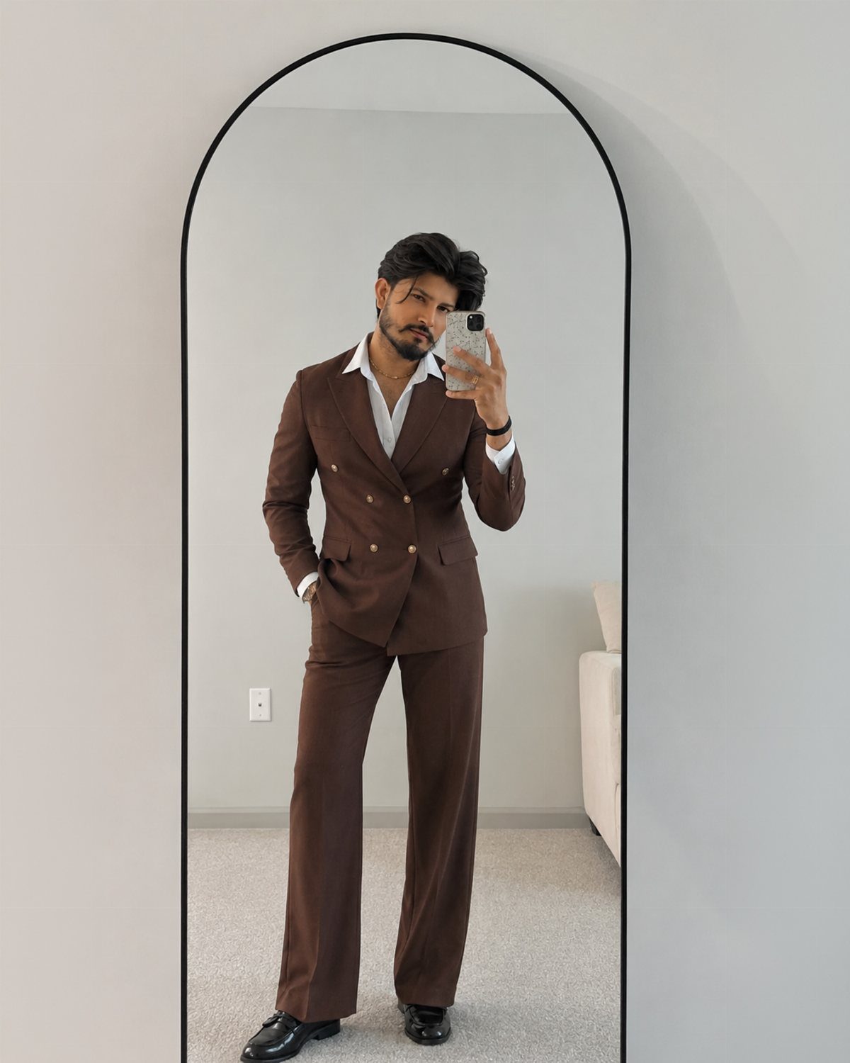 Man in a brown double-breasted suit and white shirt posing in an arched mirror.