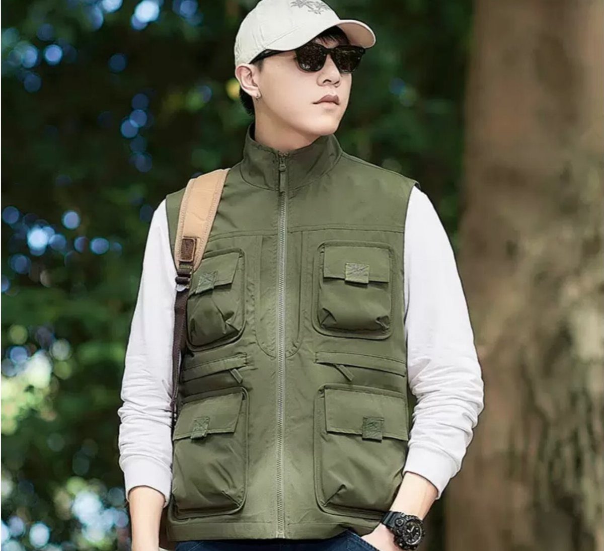 A man wearing a beige cap, sunglasses, and an olive green utility vest with multiple pockets.