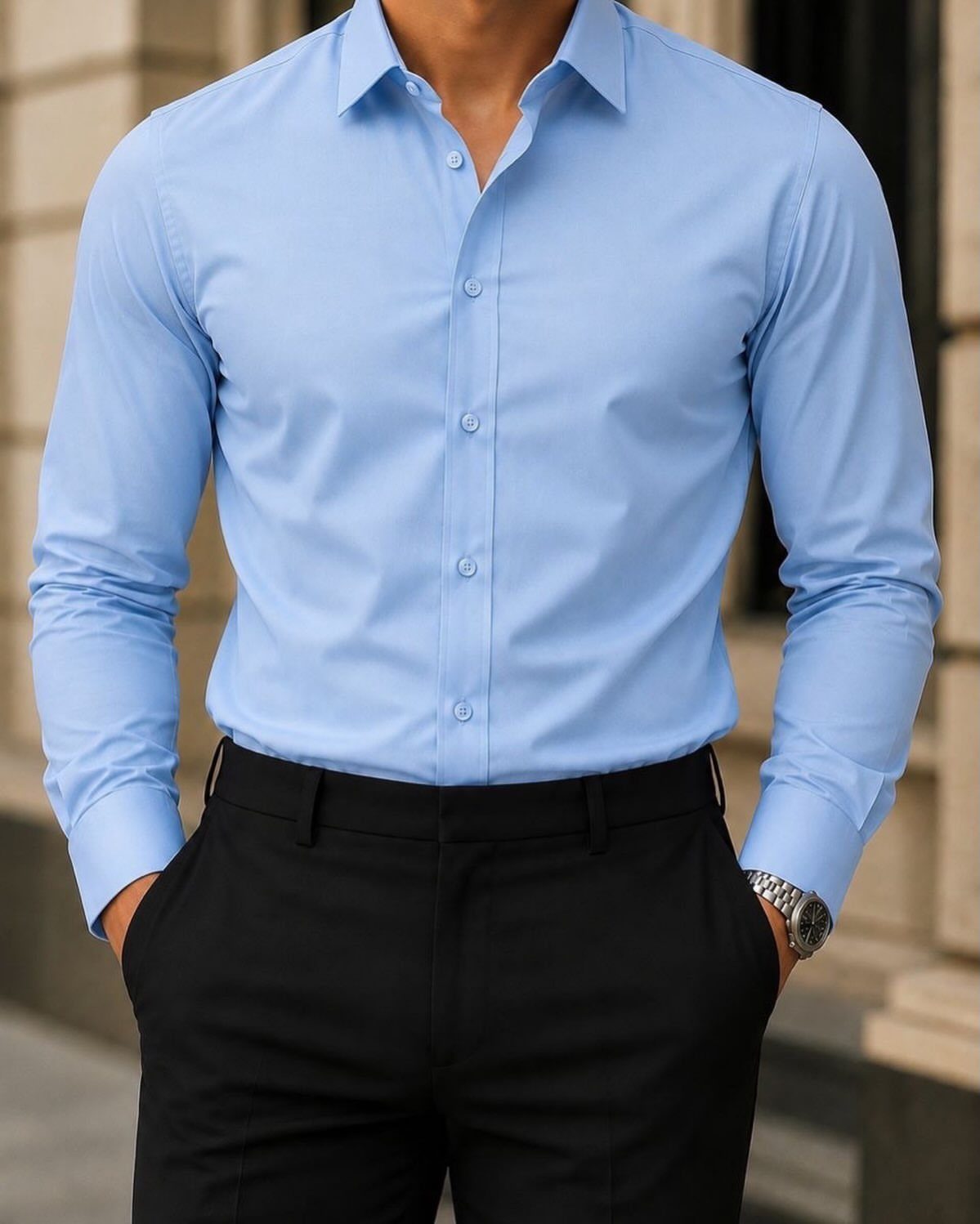A man wearing a light blue dress shirt tucked into black trousers.
