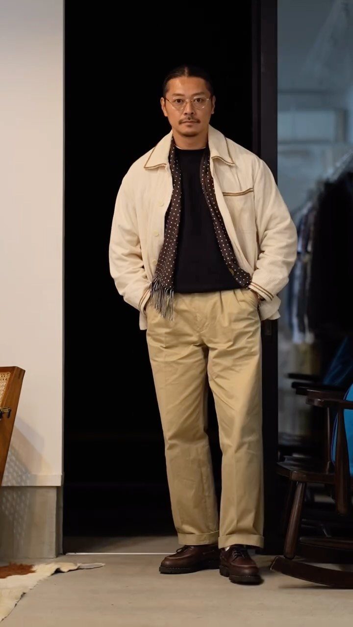 Man standing in a doorway wearing a cream jacket and tan chino trousers.