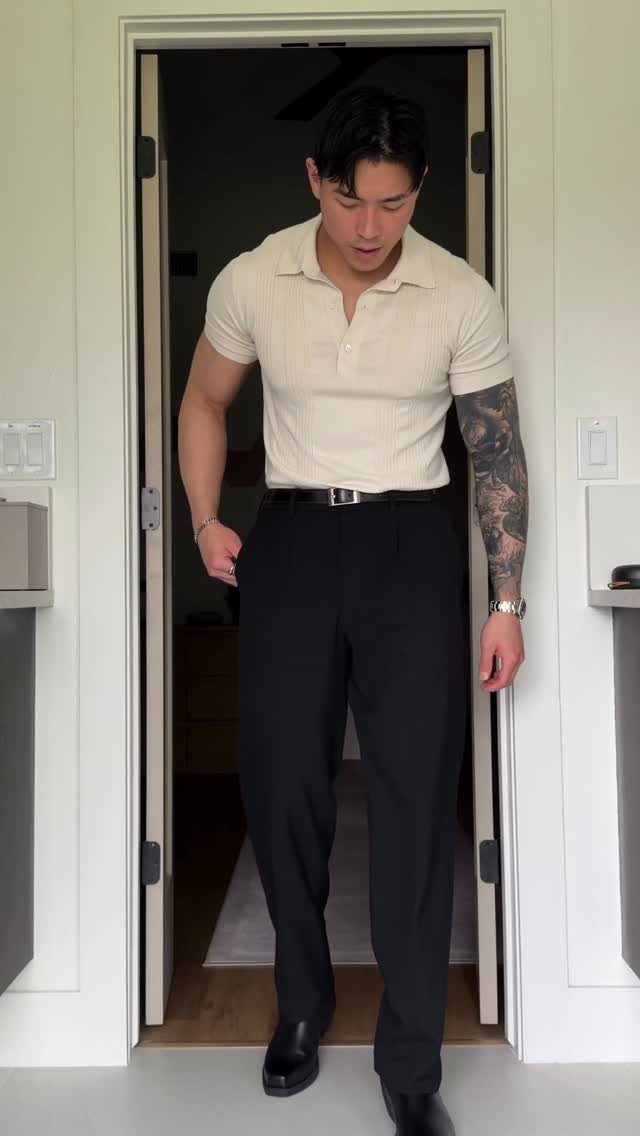 Man in a cream polo shirt and black trousers standing in a doorway.