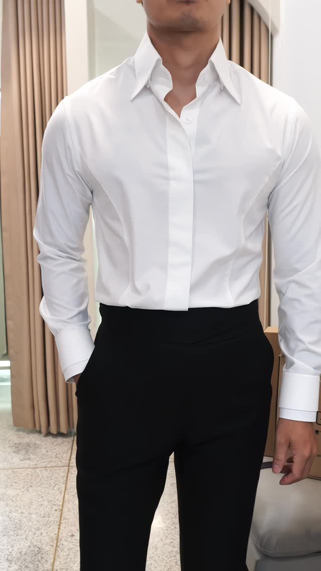 Man wearing a white button-down shirt and black trousers standing in a room.