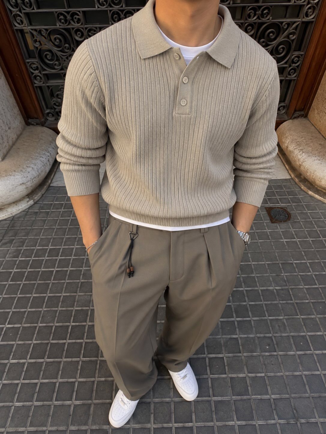 A person wearing a beige ribbed polo sweater and olive green trousers with white sneakers.