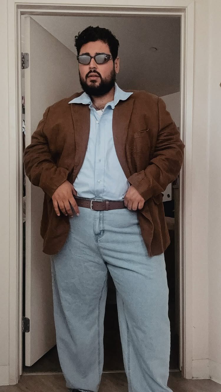A bearded man in a brown blazer and light blue shirt posing in a doorway.