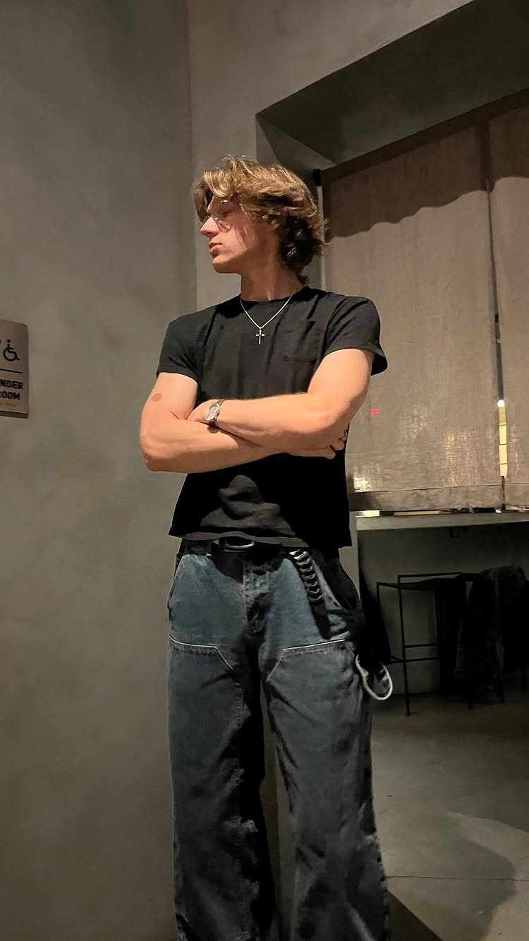 Young man posing in a black t-shirt and dark blue wide-leg jeans.