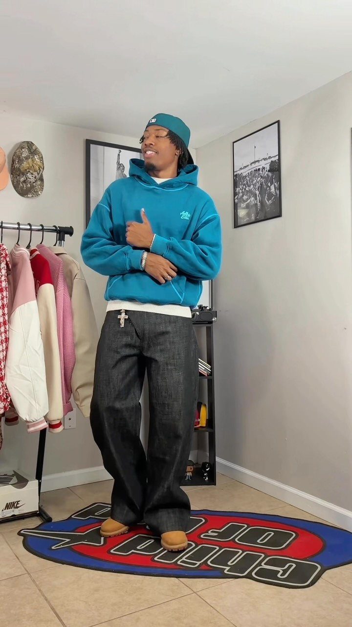 Man wearing a bright blue hoodie and baggy black denim jeans standing in a room.
