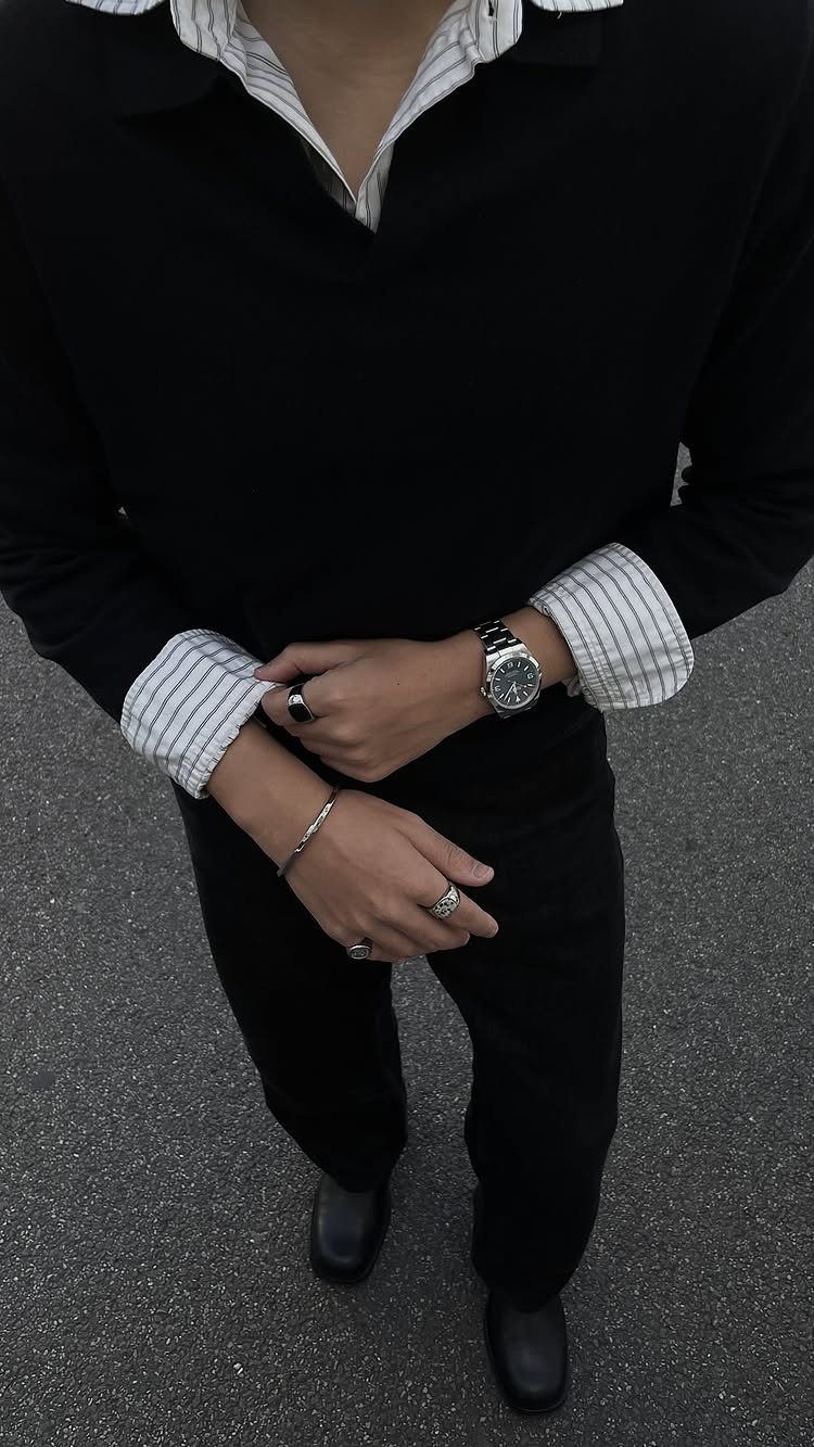 A person wearing a black polo shirt, striped undershirt, black trousers, and a silver watch.