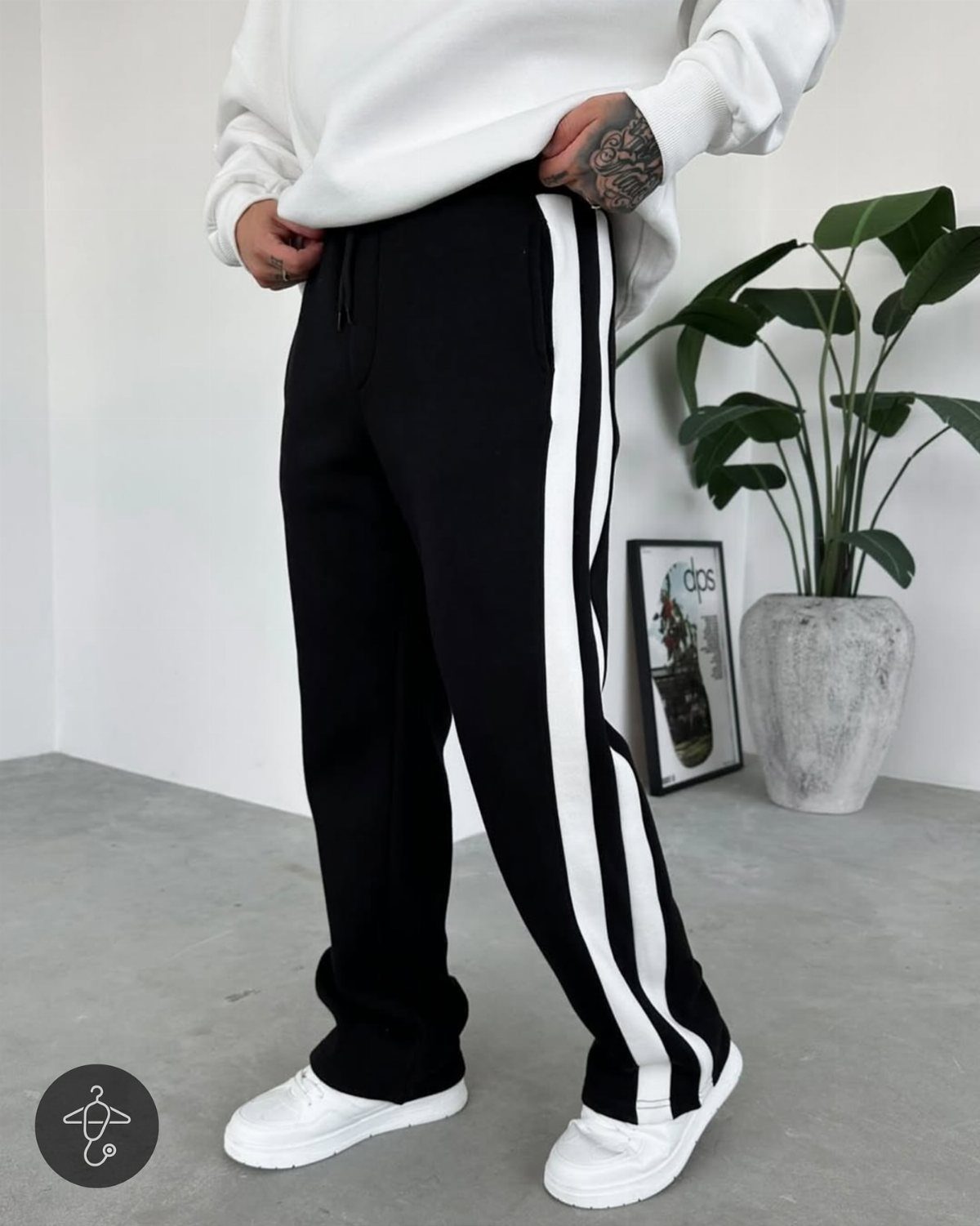 Person wearing a white sweatshirt, black striped sweatpants, and white sneakers standing indoors.