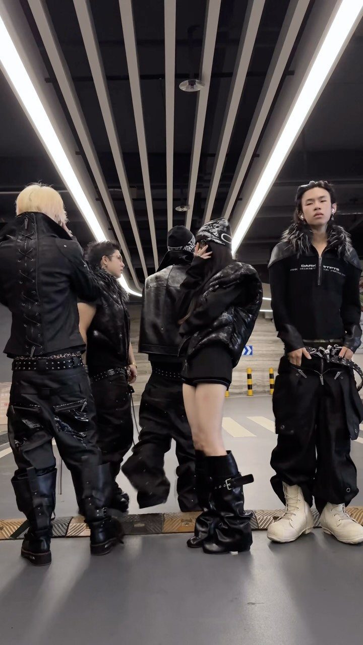 Five young people posing in an underground parking garage wearing various black streetwear outfits.