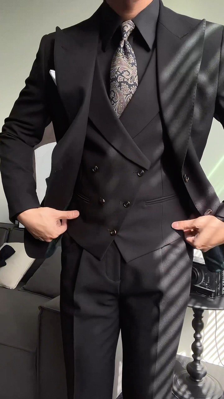 A person wearing a formal black three-piece suit with a patterned tie.