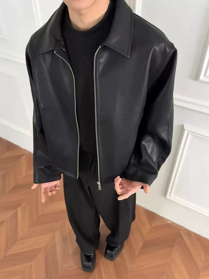 A person wearing an oversized black leather jacket, black t-shirt, and black trousers.