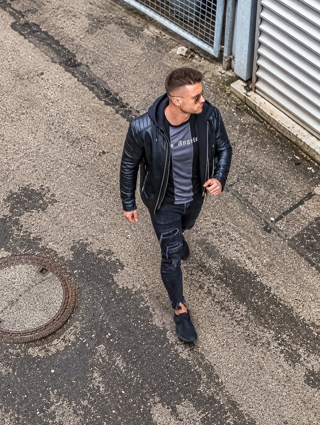 Man walking outdoors wearing a black leather jacket and black ripped skinny jeans.