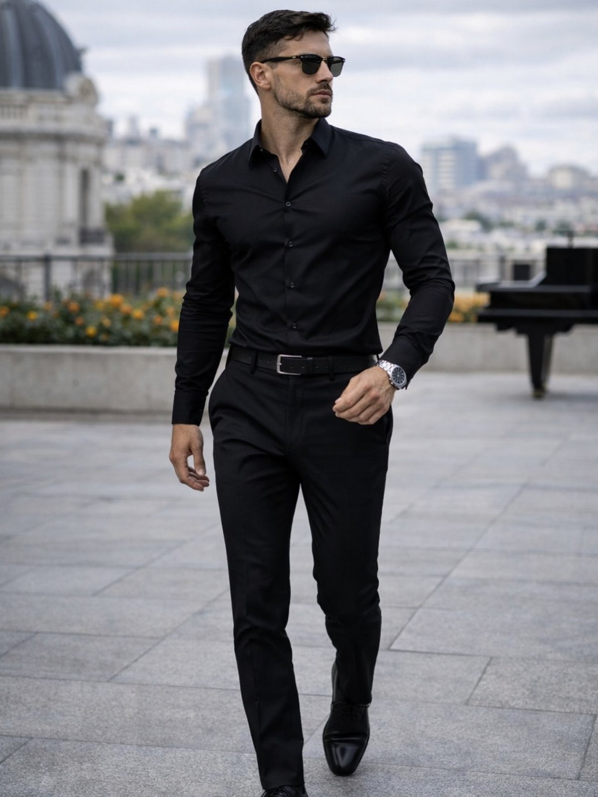 Man in a black button-down shirt and black trousers walking through an urban outdoor setting.