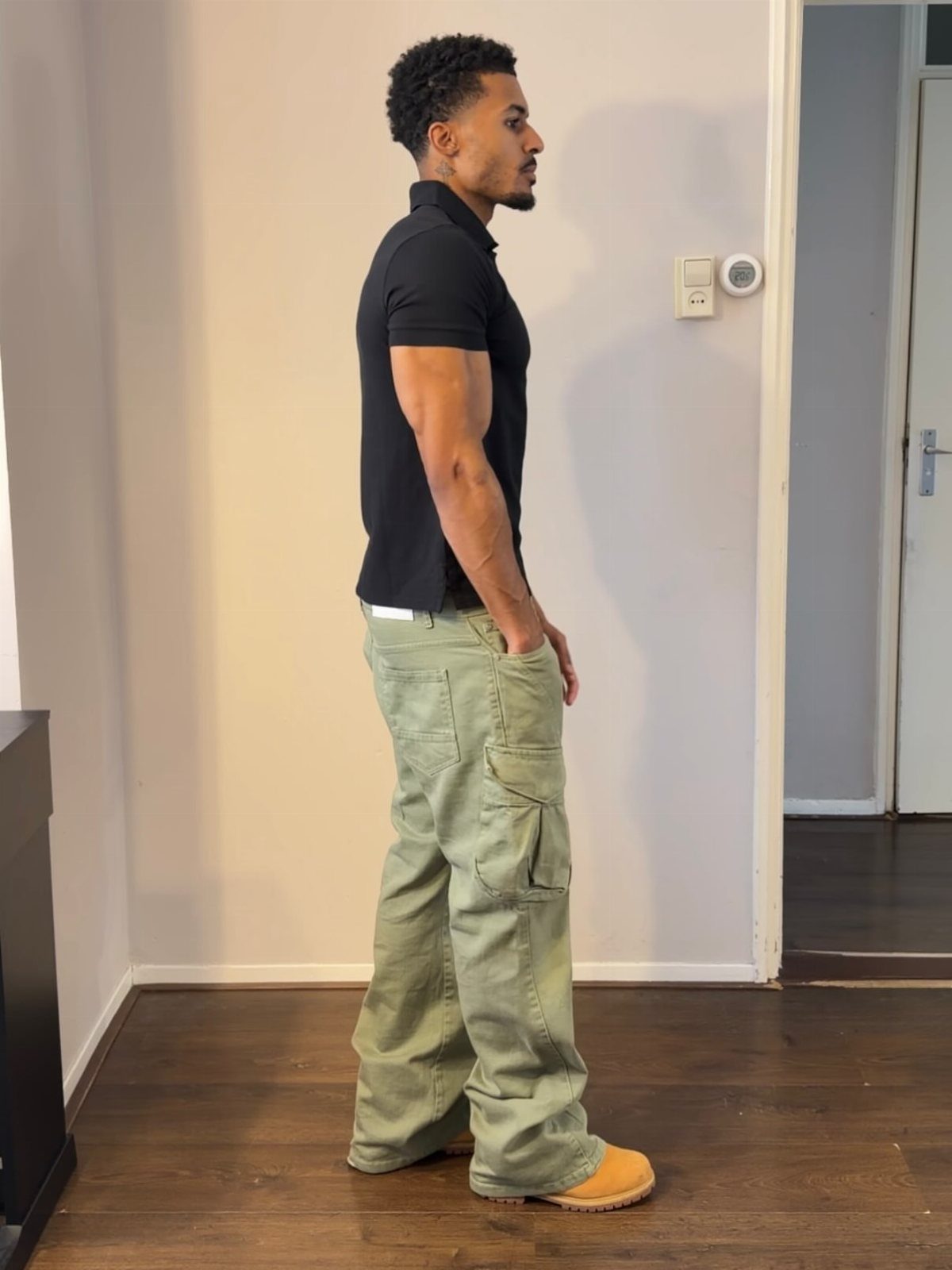 A man posing in a black polo shirt and baggy olive green cargo pants.