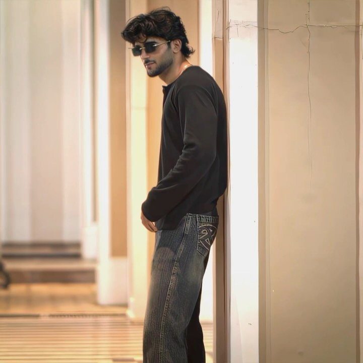 Man in a black long-sleeved shirt and blue jeans leaning against a wall.
