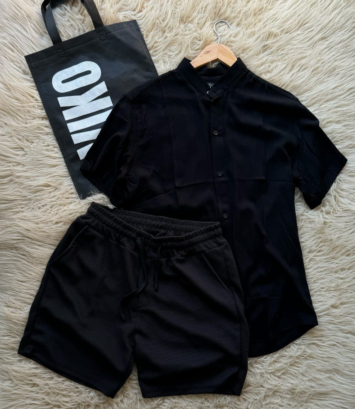Black short-sleeved shirt and black mesh shorts laid on a white textured rug.