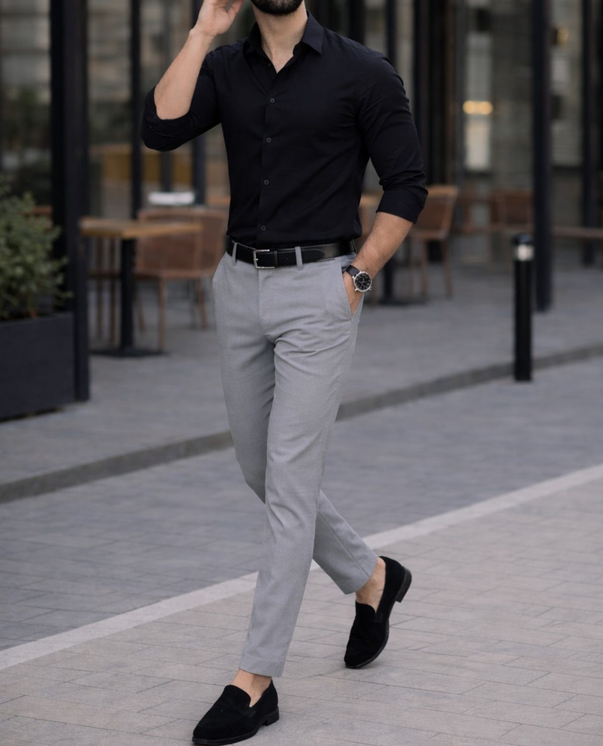 Man walking in a black button-down shirt and light grey chinos with black loafers.