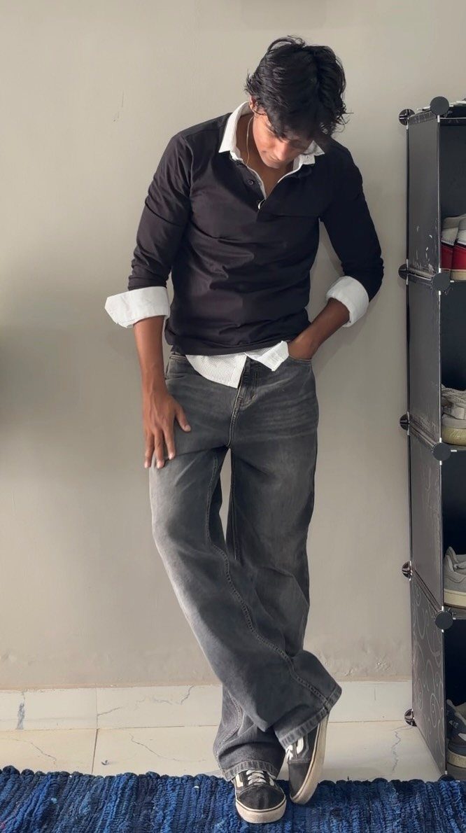 Man wearing a black shirt with white collar and cuffs, paired with baggy grey jeans.