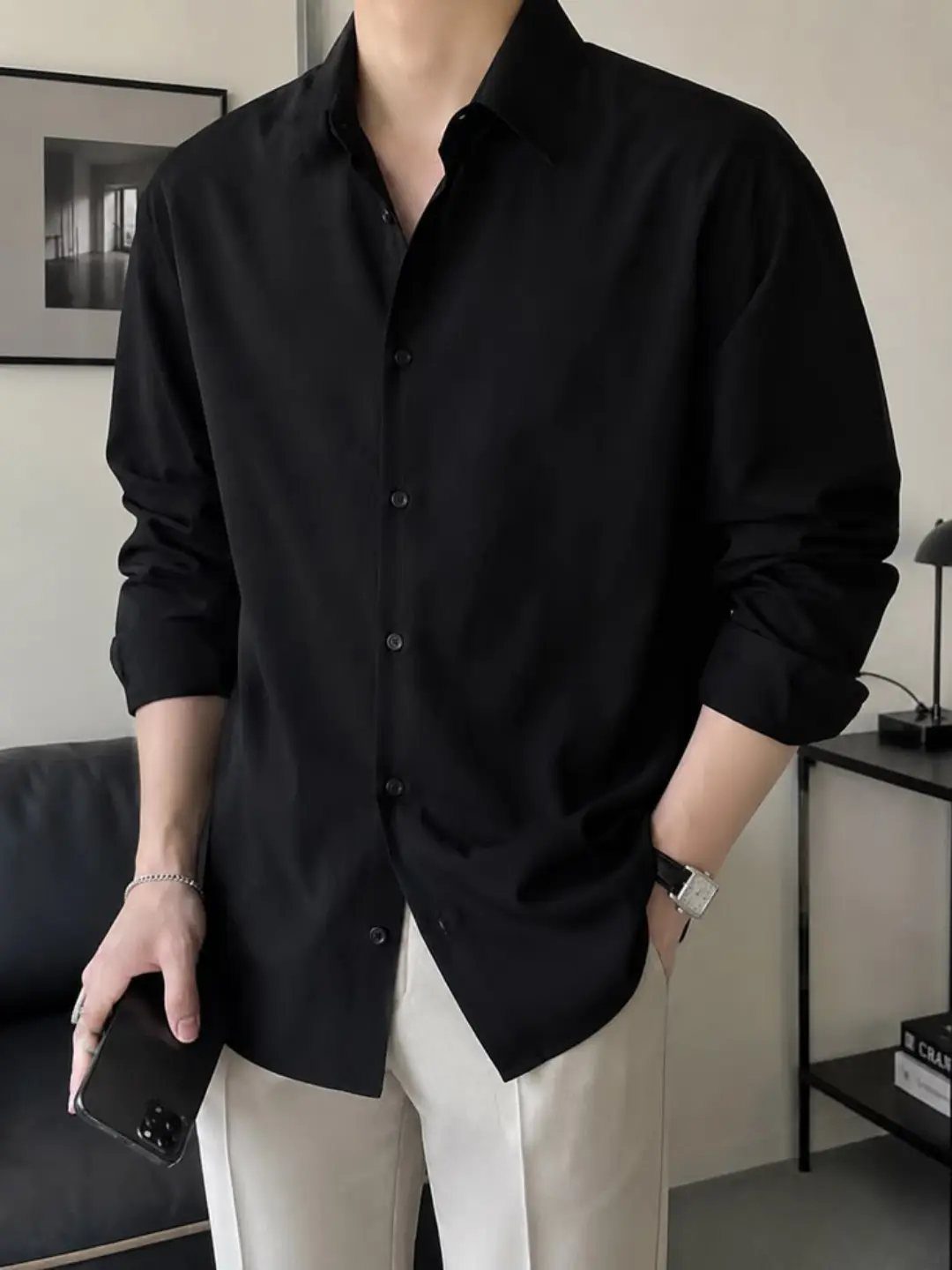 A person wearing a black button-down shirt paired with off-white trousers.