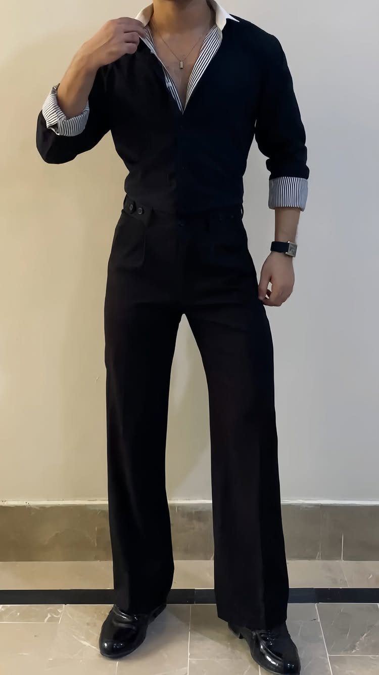 A person wearing a black shirt tucked into black trousers with patterned collar and cuffs.