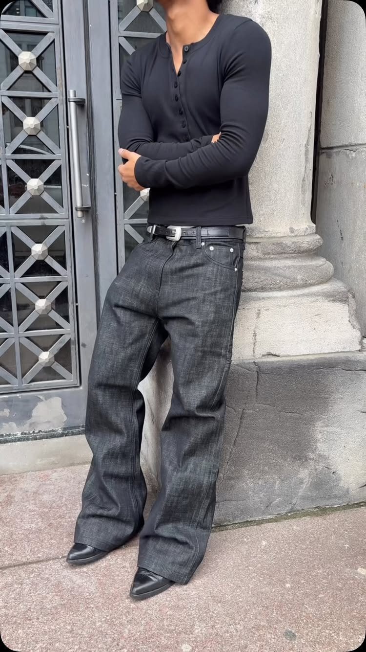 Man in a black long-sleeved shirt and wide-leg dark jeans wearing black leather boots.