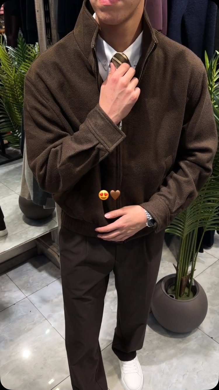 A person wearing a brown jacket, brown trousers, white shirt, and white sneakers.