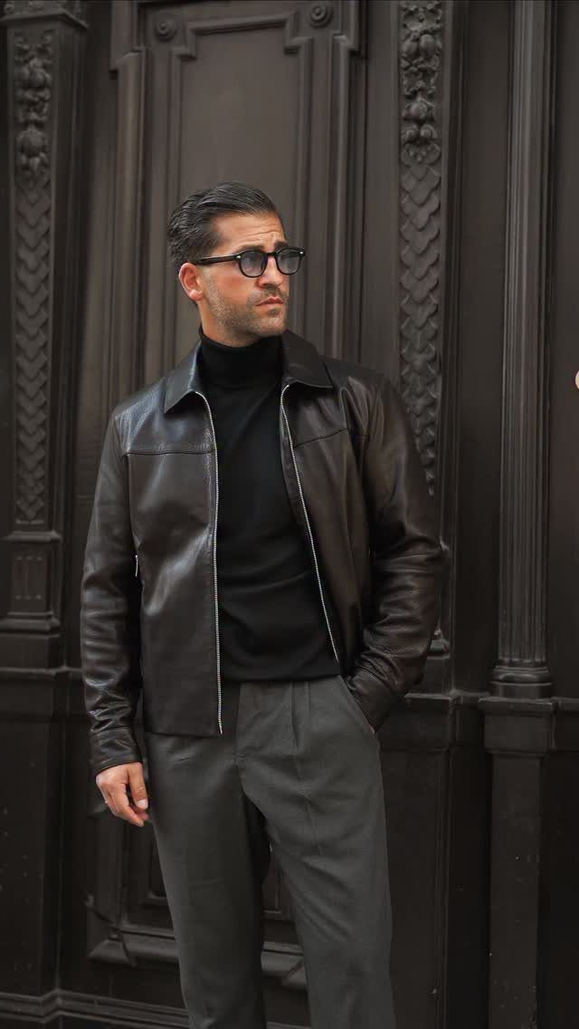 Man wearing a dark brown leather jacket and a black turtleneck with grey trousers.