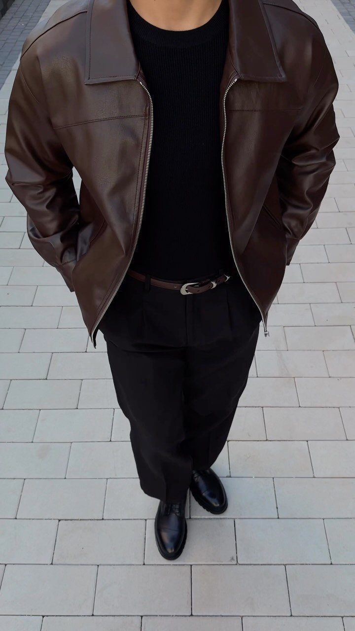 Person wearing a brown leather jacket with a black t-shirt and black trousers on a tiled ground.