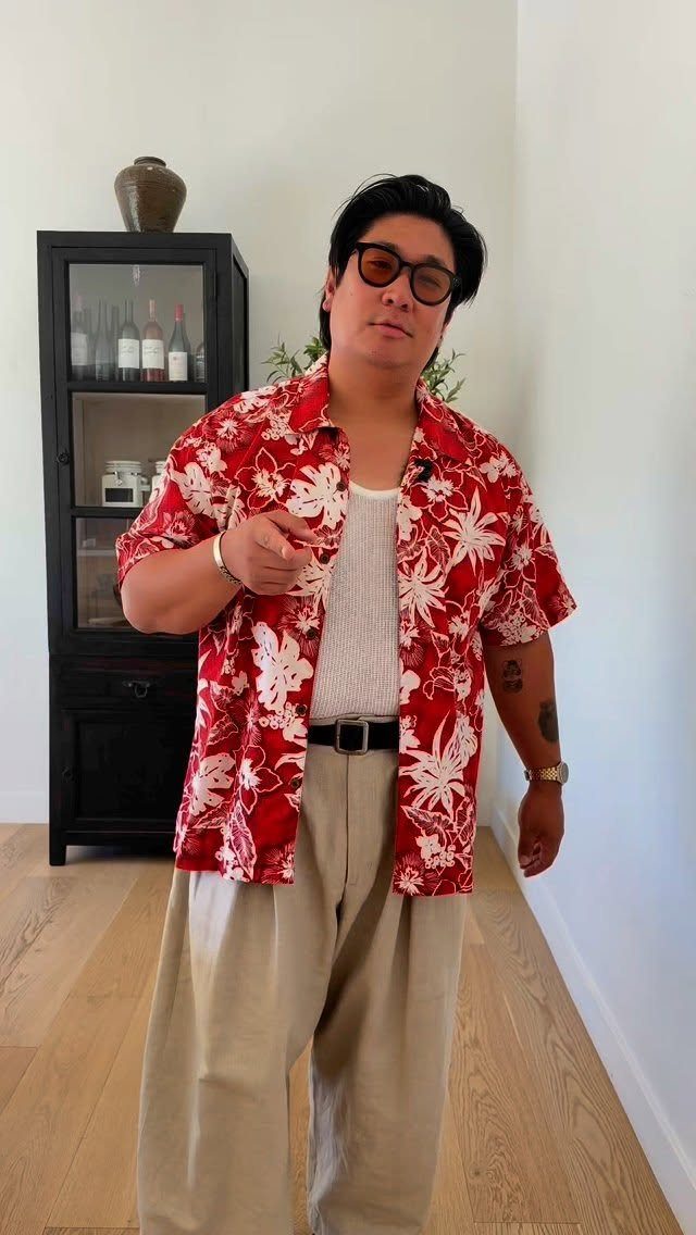 A man posing in a red and white floral Hawaiian shirt and beige trousers.