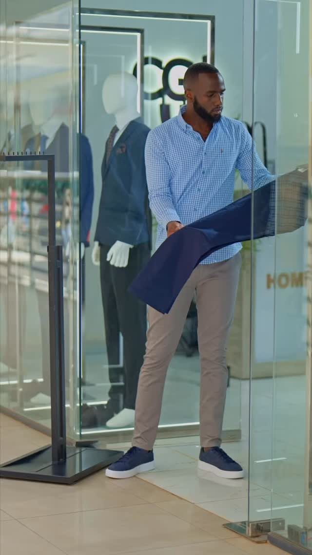 A man wearing tan chinos and a blue patterned shirt stands in a clothing store.