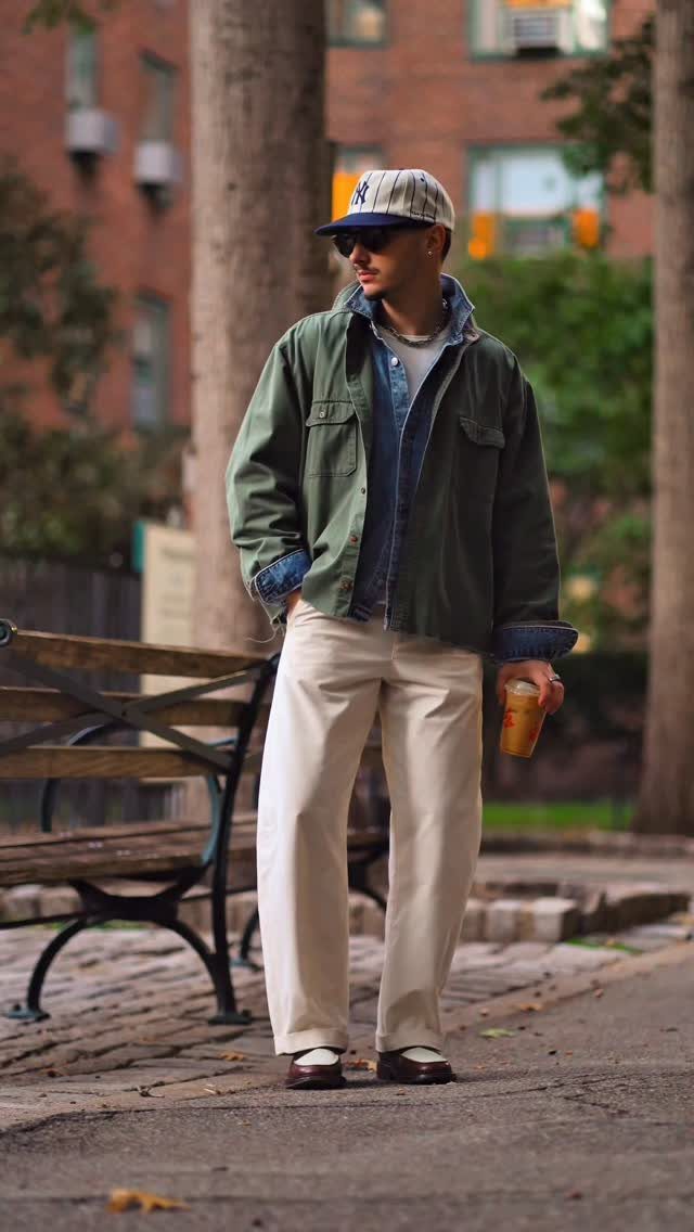 A man in a green jacket and cream trousers wearing dark loafers while standing outdoors.