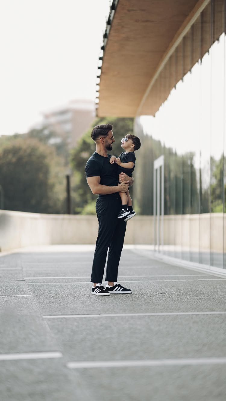 A man in black clothing holding a small child while standing on a modern outdoor walkway.
