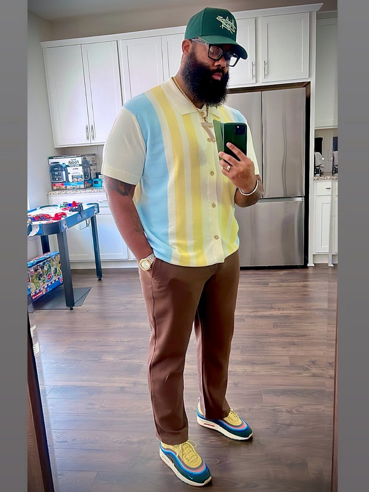 Man in a pastel striped shirt, brown pants, and colorful sneakers posing in a kitchen.