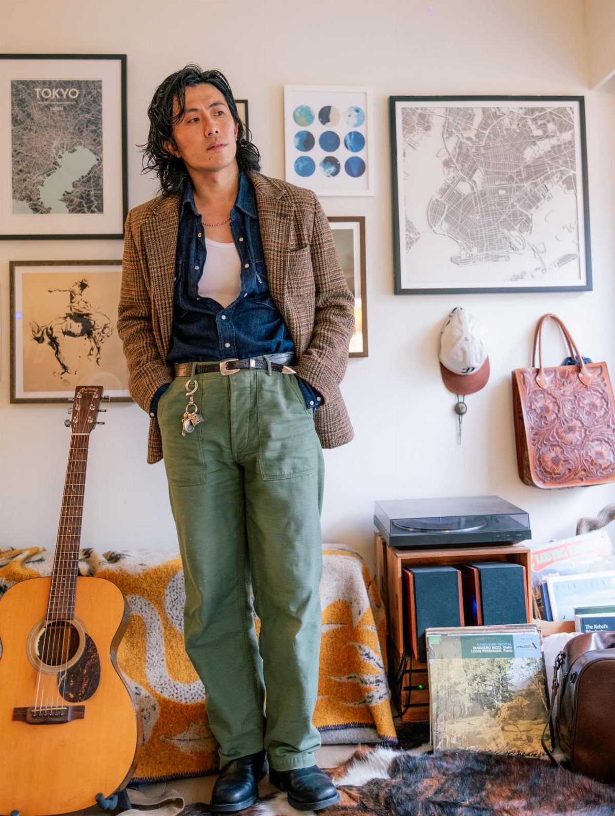 Man wearing a denim shirt, white tank top, and green cotton trousers standing in a room.