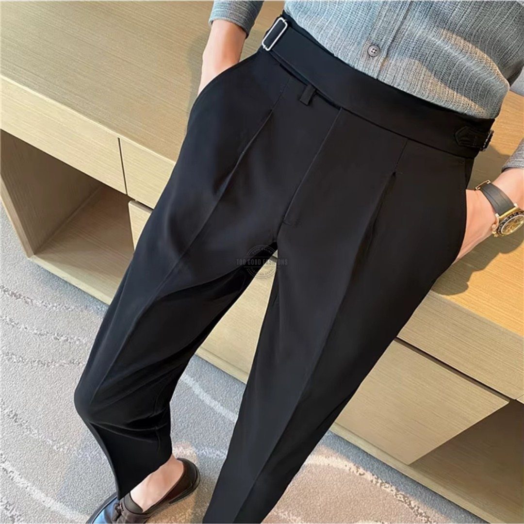 A person wearing black high-waisted trousers and a grey shirt leaning against a wooden bench.