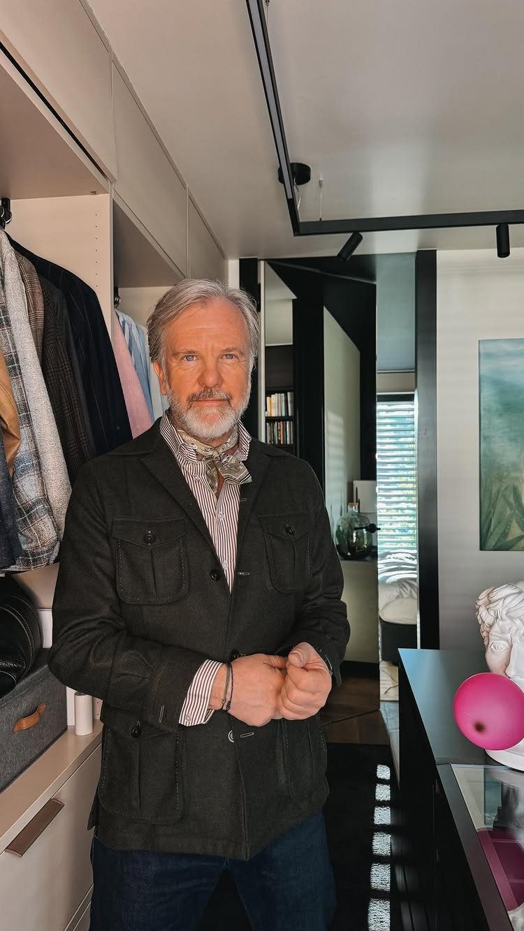 Man with grey hair wearing a dark olive green utility jacket and a patterned scarf.