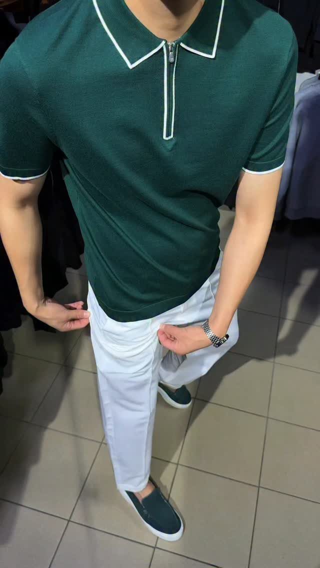Man wearing a dark green polo shirt with white trim and white trousers.