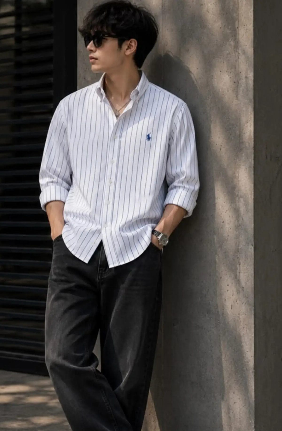 A man in a striped shirt and black trousers leaning against a concrete wall.