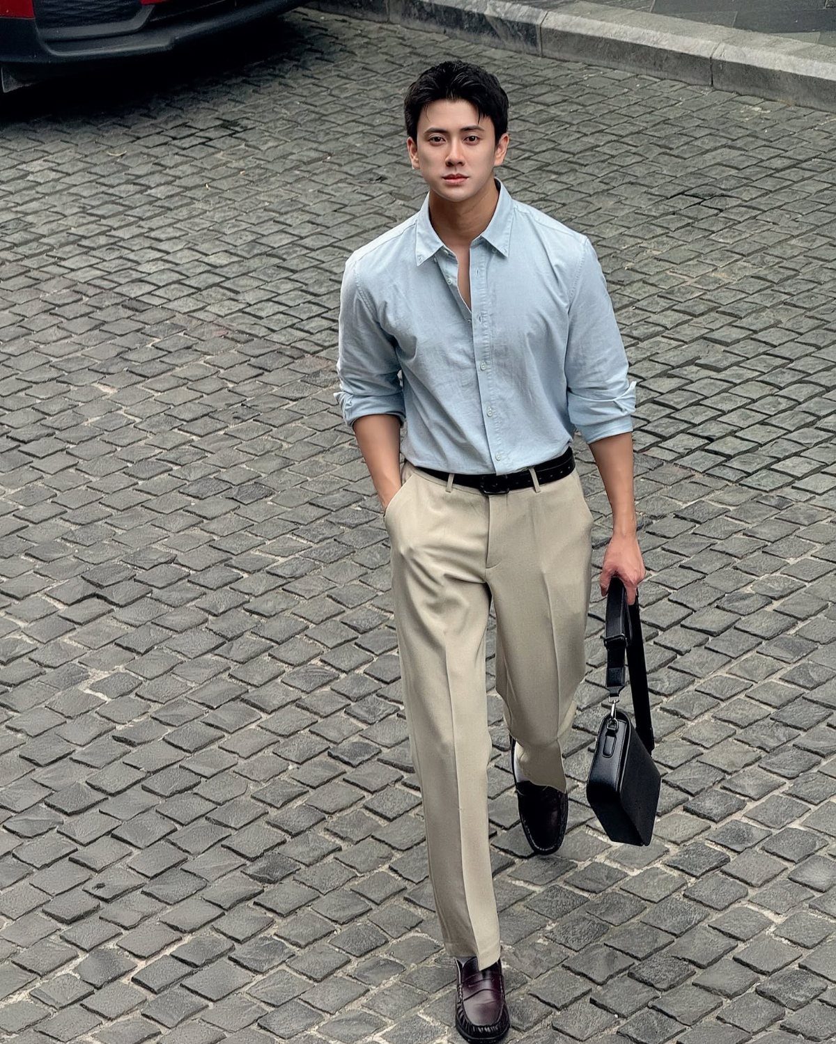 Man walking on cobblestones wearing a light blue shirt and beige trousers.