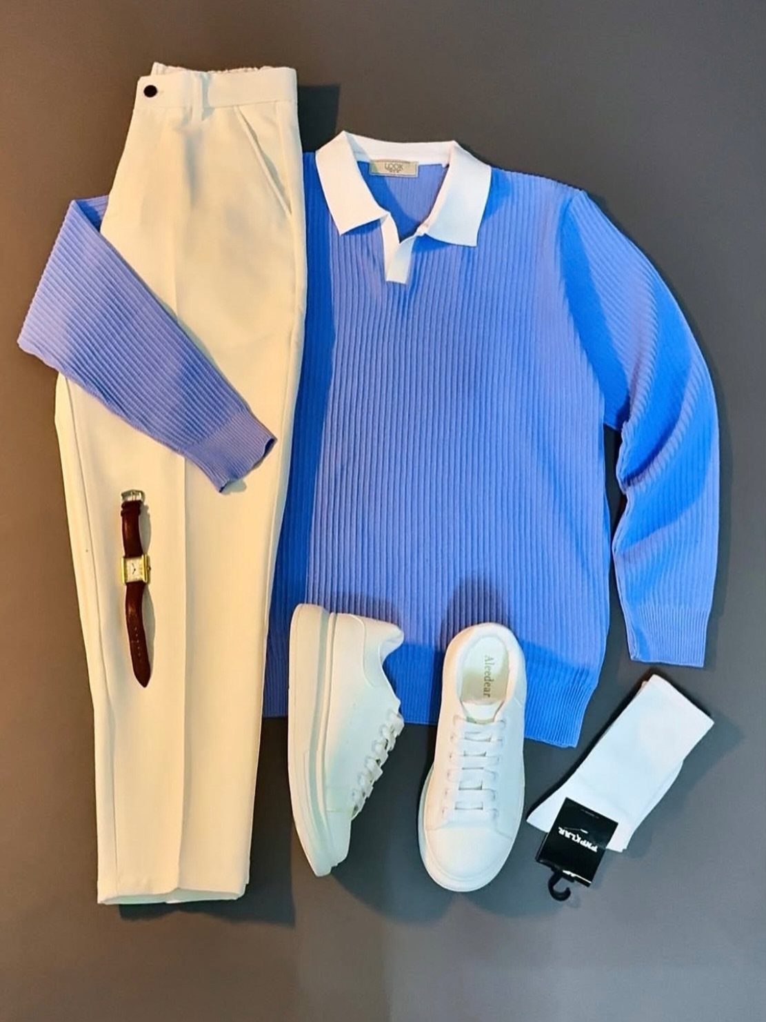 A blue polo shirt, white trousers, white sneakers, and a brown belt laid out flat.