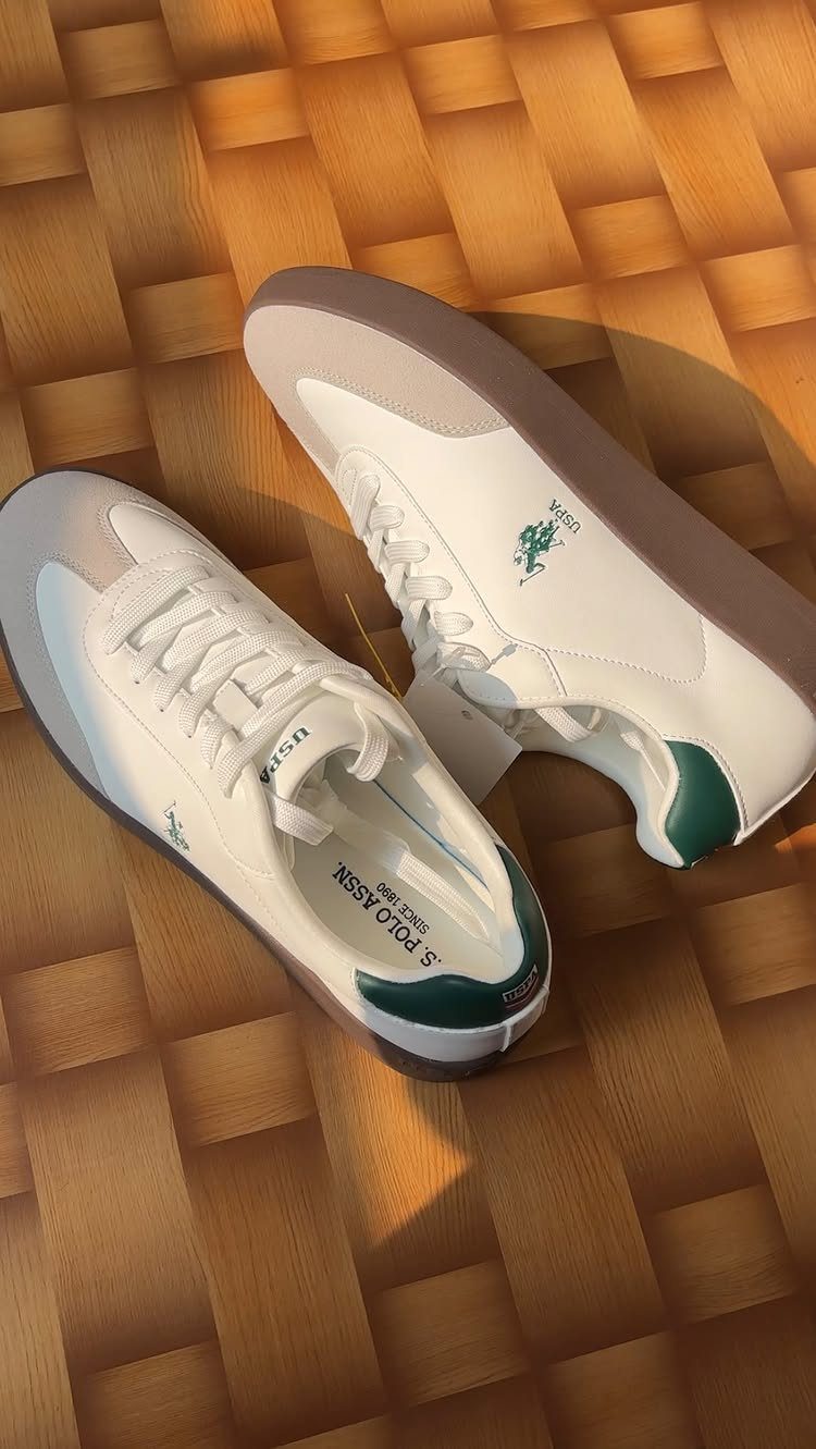 White and beige low-top sneakers with green heel accents resting on a wooden parquet floor.