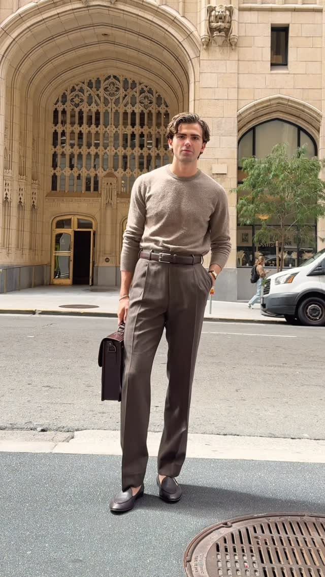 A man wearing a beige sweater and brown trousers standing on a city street.