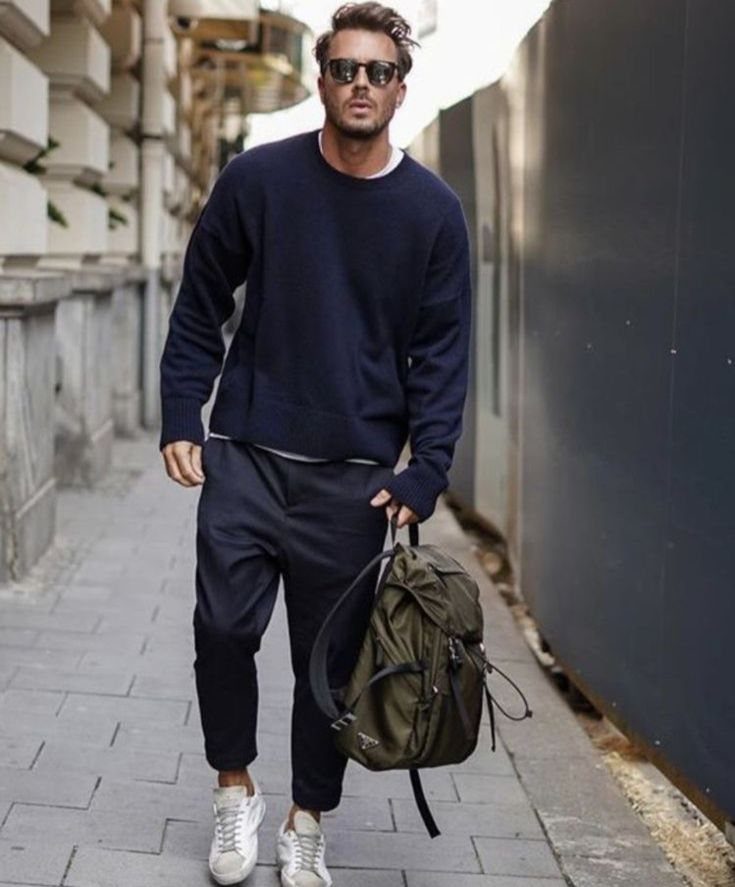 Man in navy sweatshirt and dark trousers walking through a city street with a backpack.