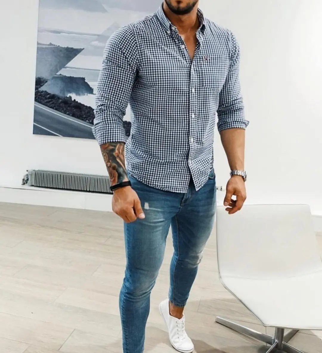 A muscular man posing in a fitted checkered shirt, tight blue jeans, and white sneakers.