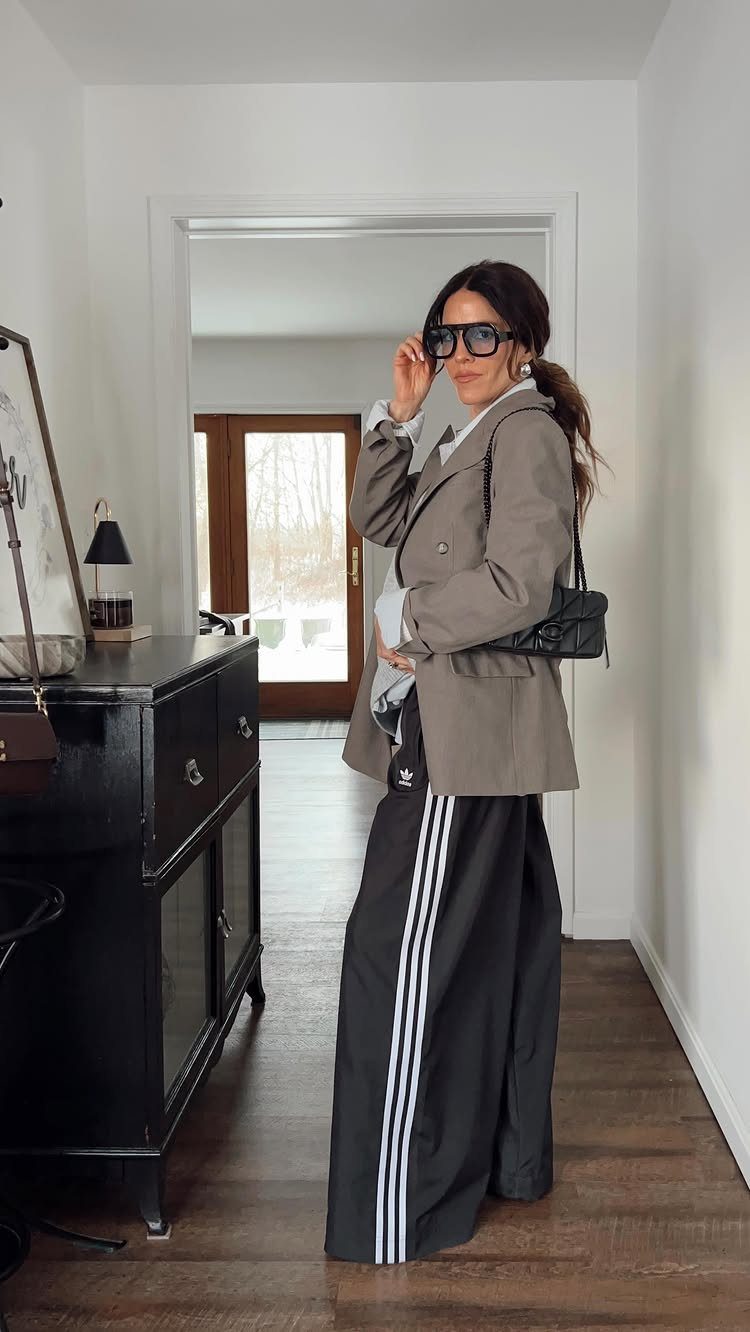 Woman posing in a tan blazer and black Adidas wide-leg track pants with white stripes.