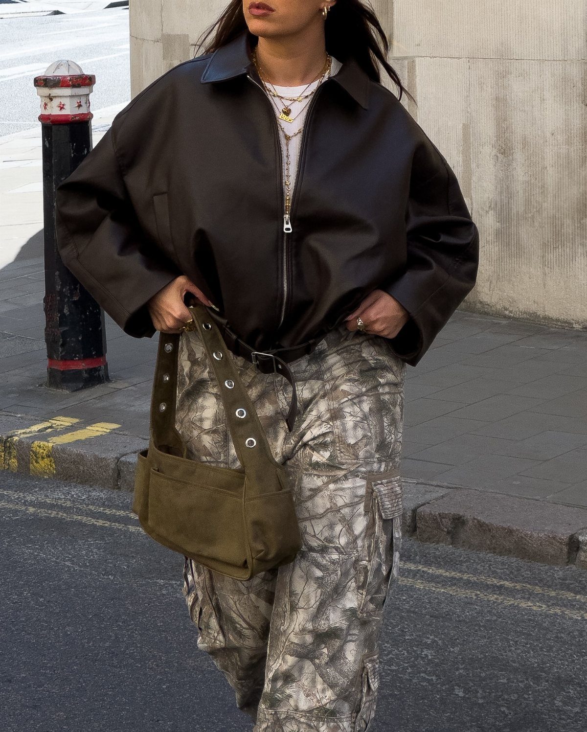 A person walking in an oversized brown leather jacket and camouflage cargo pants.